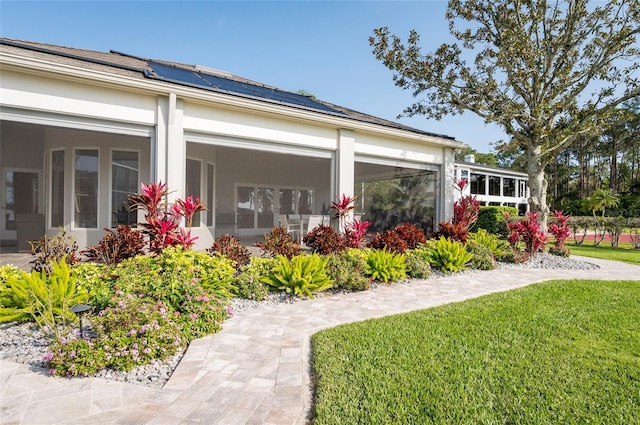 exterior space featuring a yard, roof mounted solar panels, a sunroom, and stucco siding