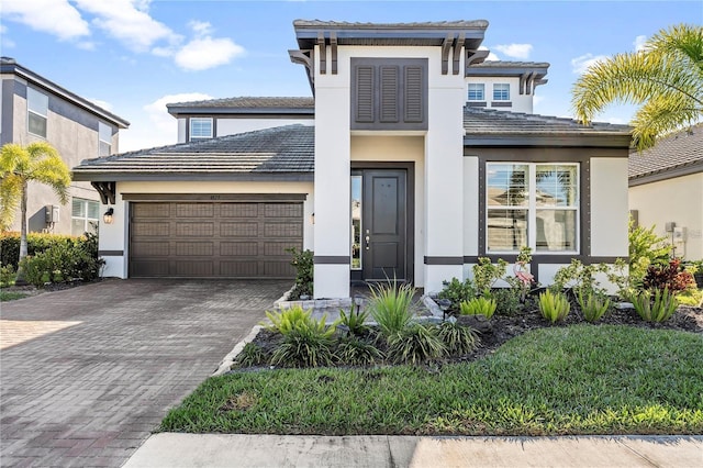 prairie-style home with a garage, decorative driveway, and stucco siding