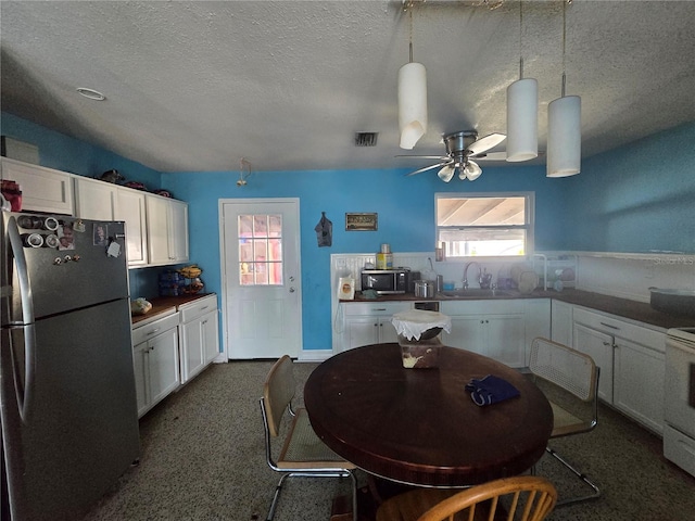 kitchen featuring stainless steel microwave, freestanding refrigerator, white cabinets, a sink, and a textured ceiling