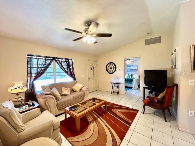 living room with a ceiling fan, visible vents, vaulted ceiling, and light tile patterned floors