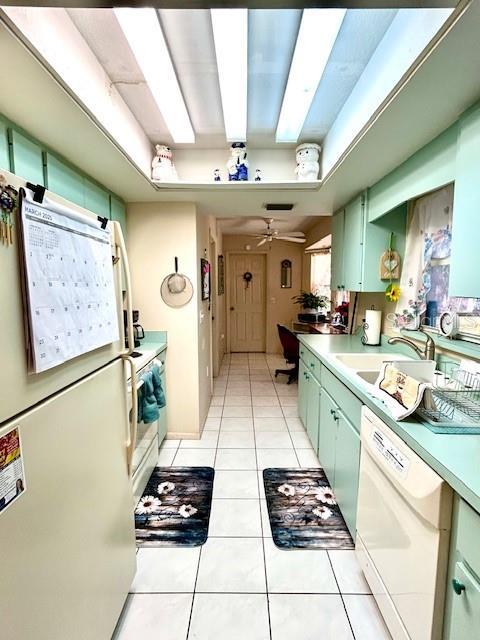 kitchen featuring white appliances, light tile patterned flooring, a sink, and green cabinets