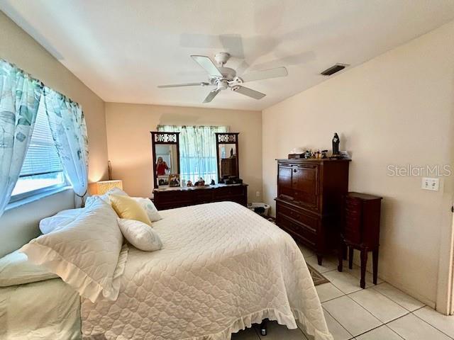 bedroom with light tile patterned floors, ceiling fan, multiple windows, and visible vents