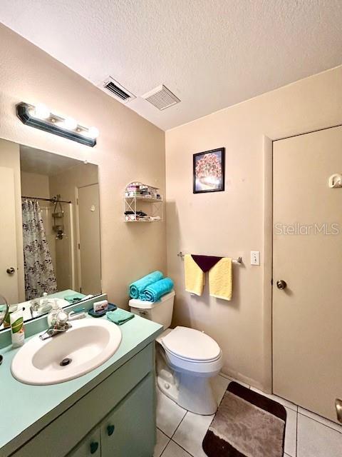 full bathroom with a textured ceiling, tile patterned flooring, toilet, vanity, and visible vents