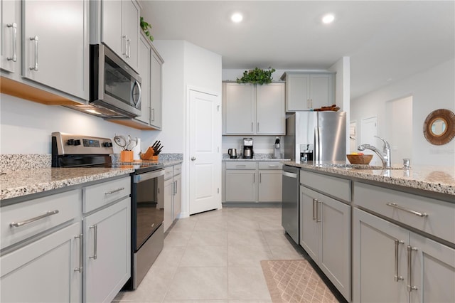 kitchen with light tile patterned floors, gray cabinets, appliances with stainless steel finishes, and a sink