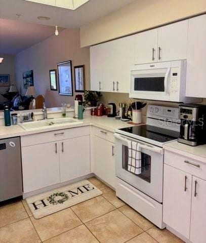 kitchen with light countertops, white appliances, a sink, and white cabinetry