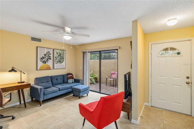 living room with baseboards, visible vents, light tile patterned flooring, ceiling fan, and a textured ceiling