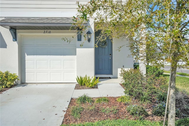 doorway to property featuring stucco siding, a garage, and roof with shingles