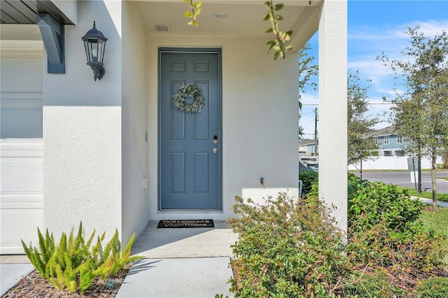 doorway to property with visible vents, stucco siding, and a garage