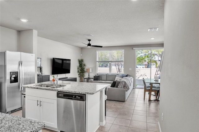 kitchen with open floor plan, light stone counters, stainless steel appliances, white cabinetry, and a sink