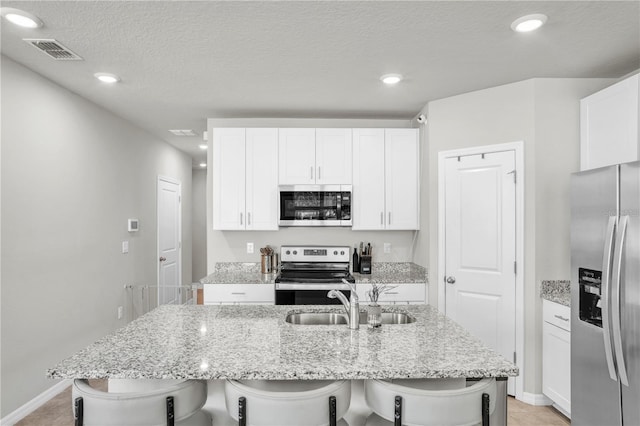 kitchen featuring a kitchen bar, visible vents, a sink, white cabinetry, and stainless steel appliances