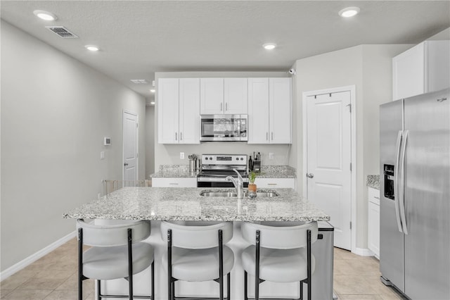 kitchen with stainless steel appliances, a kitchen breakfast bar, an island with sink, and white cabinets