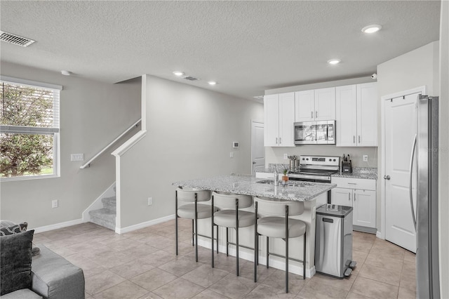 kitchen with light stone counters, visible vents, a breakfast bar, appliances with stainless steel finishes, and white cabinetry