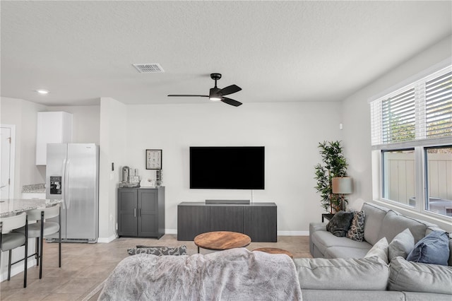 living area with light tile patterned flooring, visible vents, a textured ceiling, and ceiling fan