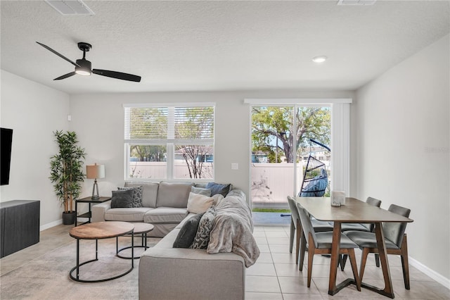 living area with baseboards, visible vents, light tile patterned flooring, ceiling fan, and a textured ceiling