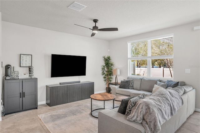 living area with visible vents, a textured ceiling, light tile patterned floors, baseboards, and ceiling fan