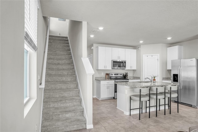 kitchen featuring light stone countertops, a center island with sink, white cabinetry, appliances with stainless steel finishes, and a kitchen bar