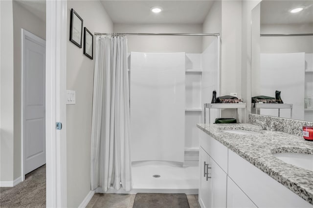 bathroom featuring a shower stall, double vanity, baseboards, and a sink