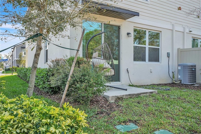 entrance to property with central AC unit, a yard, and stucco siding