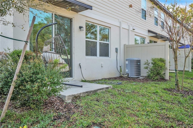 view of side of home with central air condition unit, fence, a lawn, and stucco siding