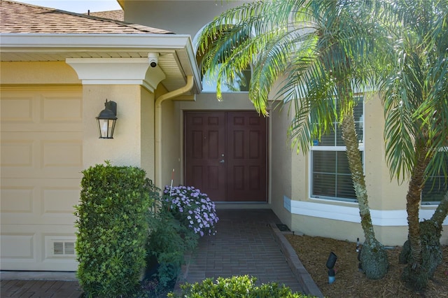 property entrance featuring a shingled roof, visible vents, a garage, and stucco siding