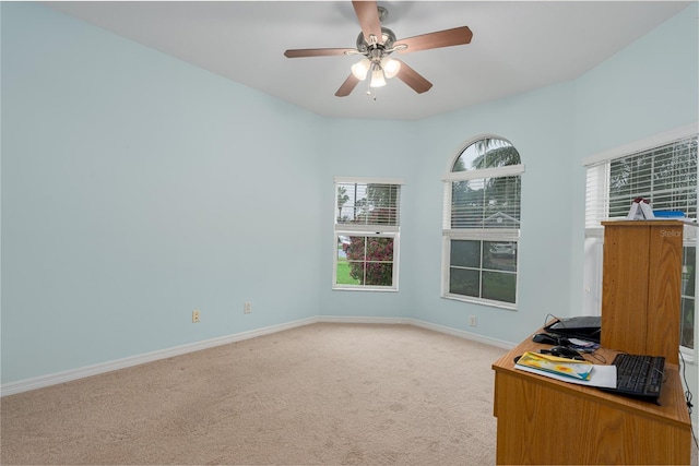 unfurnished office with light colored carpet, a ceiling fan, and baseboards