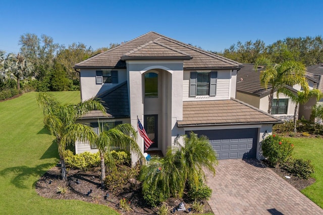 view of front of property with a tiled roof, a front yard, stucco siding, decorative driveway, and a garage