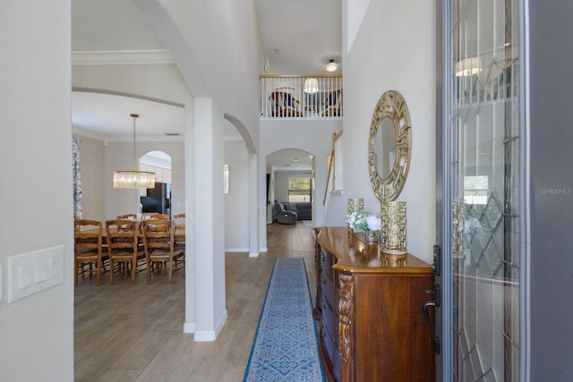 foyer entrance featuring crown molding, baseboards, an inviting chandelier, wood finished floors, and arched walkways