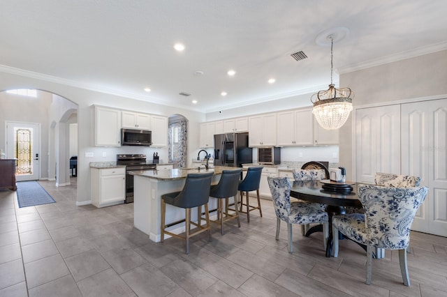 kitchen with visible vents, a center island with sink, arched walkways, white cabinets, and stainless steel appliances