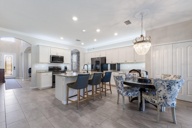 kitchen with visible vents, a breakfast bar area, appliances with stainless steel finishes, arched walkways, and a kitchen island with sink