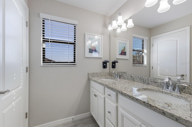 full bath with double vanity, baseboards, and a sink