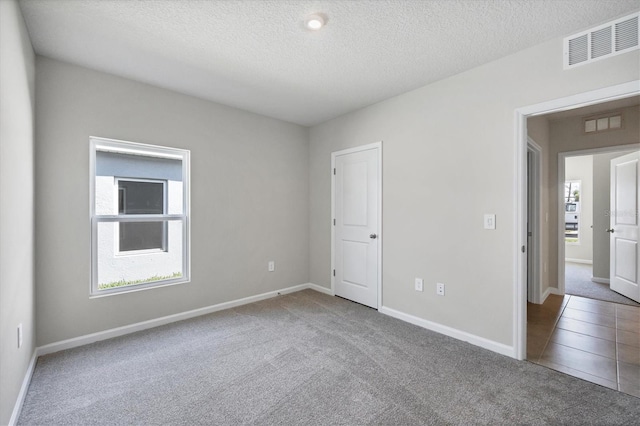 carpeted empty room with visible vents, a textured ceiling, and baseboards