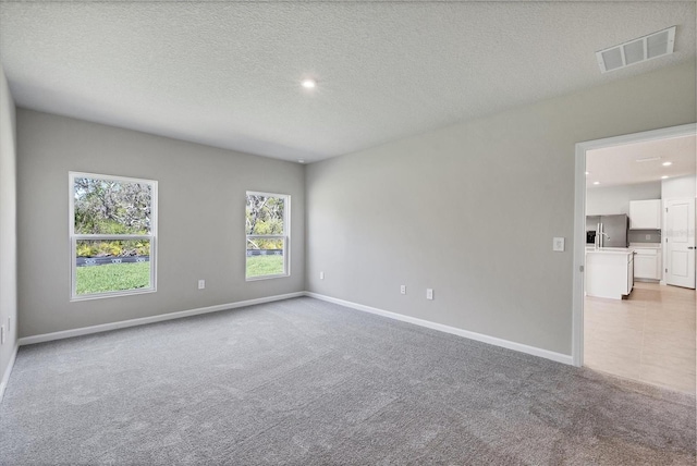 empty room featuring light carpet, visible vents, a textured ceiling, and baseboards