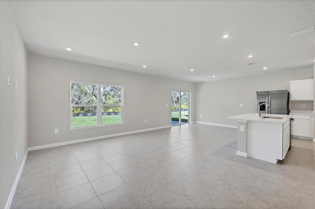 interior space with open floor plan, an island with sink, stainless steel refrigerator with ice dispenser, and a sink