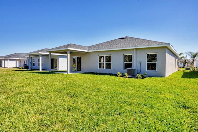 rear view of house with a yard, roof with shingles, central AC, and stucco siding