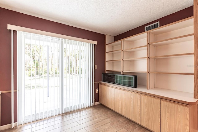 unfurnished office featuring baseboards, light wood-style floors, visible vents, and a textured ceiling