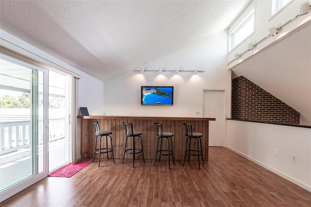 bar with a healthy amount of sunlight, a textured ceiling, a bar, and vaulted ceiling