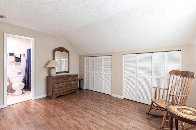 living area featuring visible vents, baseboards, lofted ceiling, light wood-style flooring, and a textured ceiling