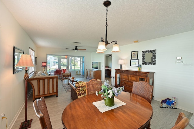 dining space featuring light wood finished floors, visible vents, baseboards, a textured ceiling, and a ceiling fan