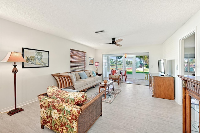 living area featuring light wood-type flooring, visible vents, a ceiling fan, a textured ceiling, and baseboards