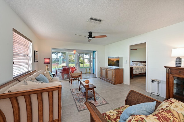 living room with light wood finished floors, visible vents, a fireplace, a textured ceiling, and a ceiling fan