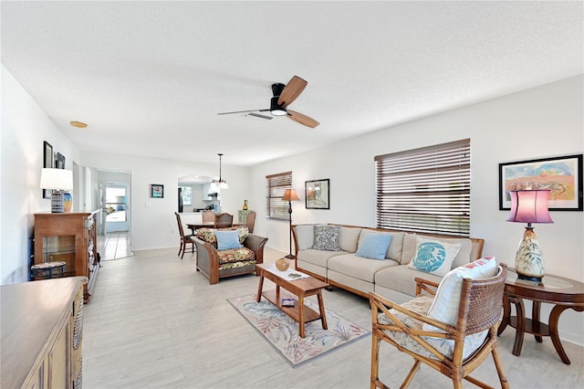 living room featuring baseboards, a textured ceiling, and ceiling fan