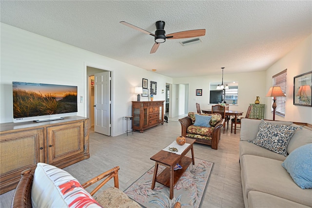 living area with visible vents, a textured ceiling, a ceiling fan, and light wood finished floors