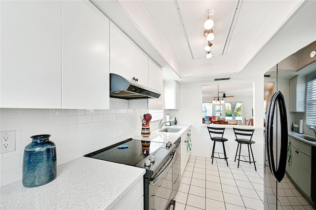 kitchen featuring electric stove, under cabinet range hood, a sink, light countertops, and a raised ceiling