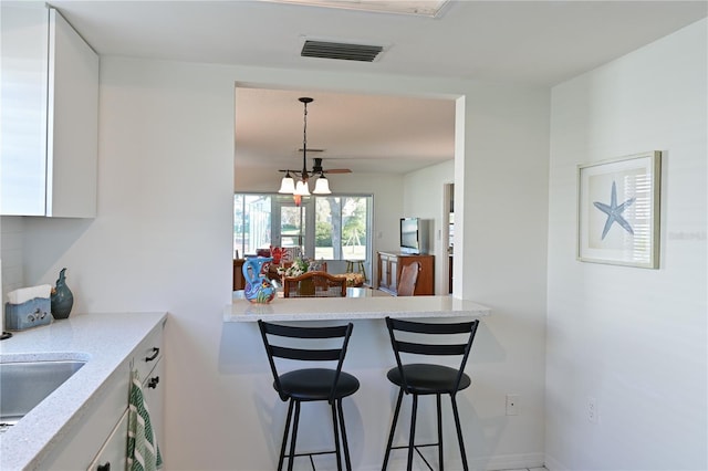 kitchen with a breakfast bar area, light stone countertops, visible vents, white cabinetry, and decorative light fixtures