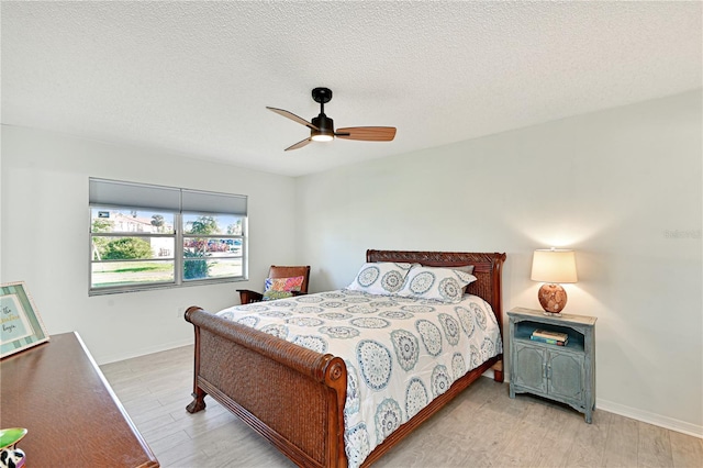 bedroom with ceiling fan, baseboards, light wood-type flooring, and a textured ceiling