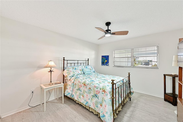 bedroom with ceiling fan, wood finished floors, baseboards, and a textured ceiling