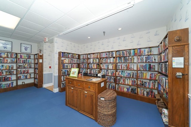 living area with bookshelves, wainscoting, wallpapered walls, and a paneled ceiling