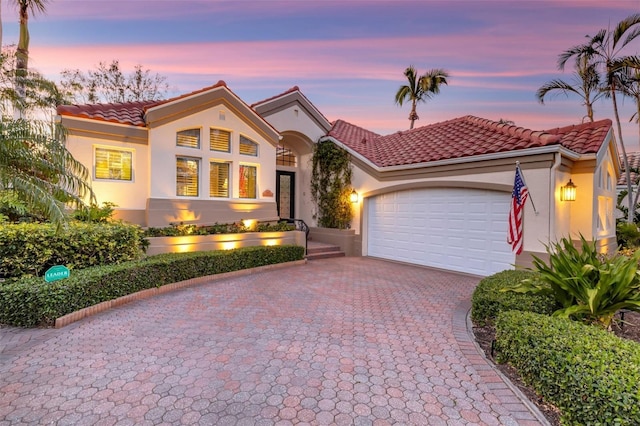 mediterranean / spanish-style house featuring stucco siding, a tiled roof, decorative driveway, and a garage