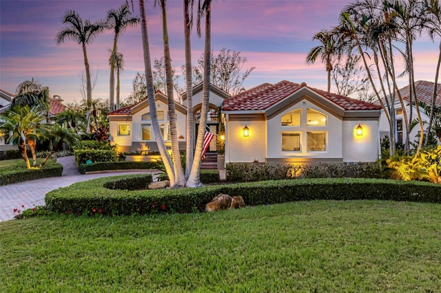 mediterranean / spanish home with a yard, stucco siding, driveway, and a tile roof