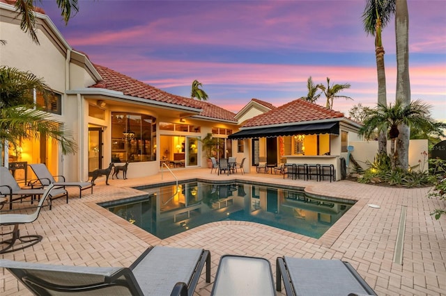 pool at dusk featuring an outdoor pool, a patio, and outdoor dry bar